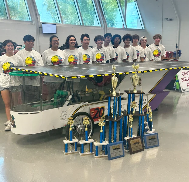 ALSET Paladins students with their solar racing car and championship trophies in the workshop